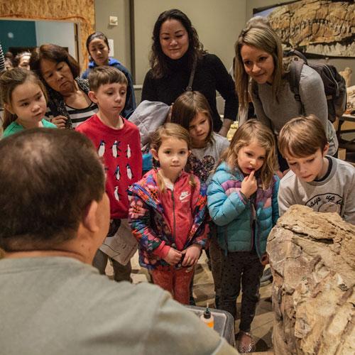 a group of kids and two women watch as fossils are prepared