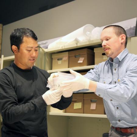 Two men wear gloves while removing an archaeological artifact from its bag