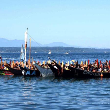 A group of decorated tribal canoes in the water with people inside the canoes