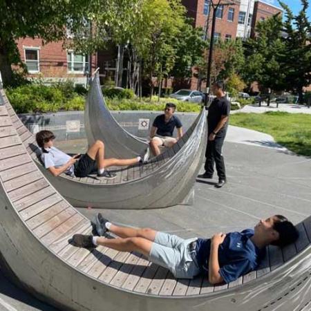 kids play on wood and metal benches that look like tatala canoes