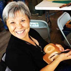 portrait of artist lou-ann neel. she is looking up at the camera and smiling as she works on a carving.