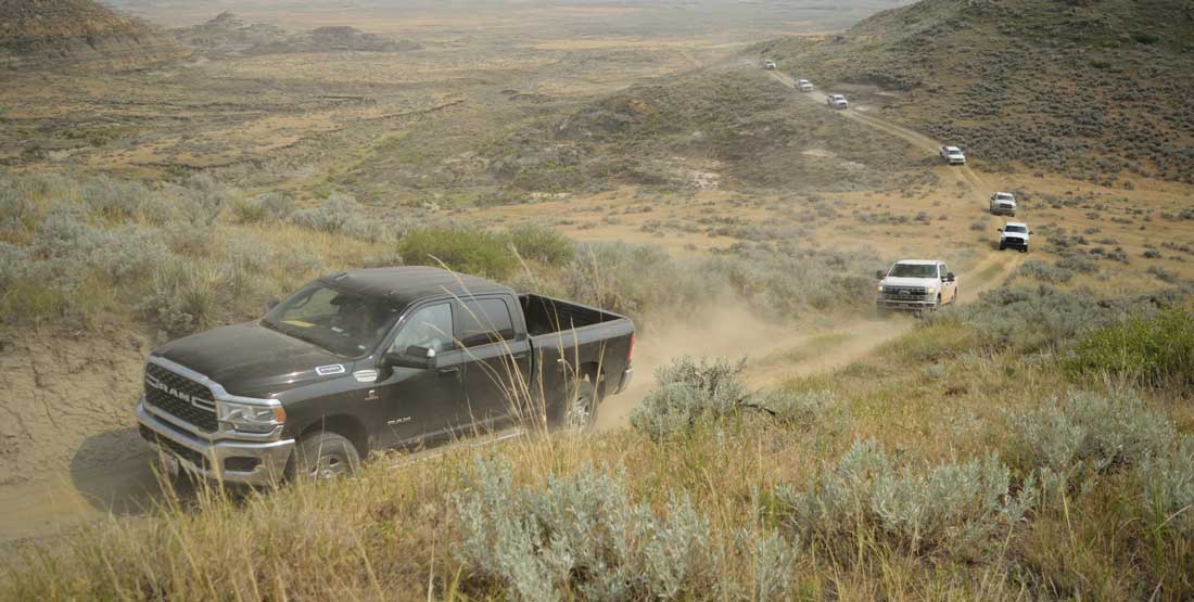 A caravan of vehicles makes their way through the dusty badlands. 