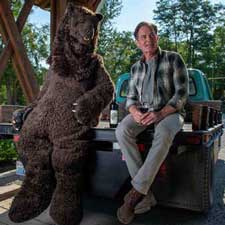 kyle maclachlan sits on the back of a truck with a giant bear sitting next to him