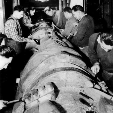 a black and white photo of a group of people carving a totem in Alaska